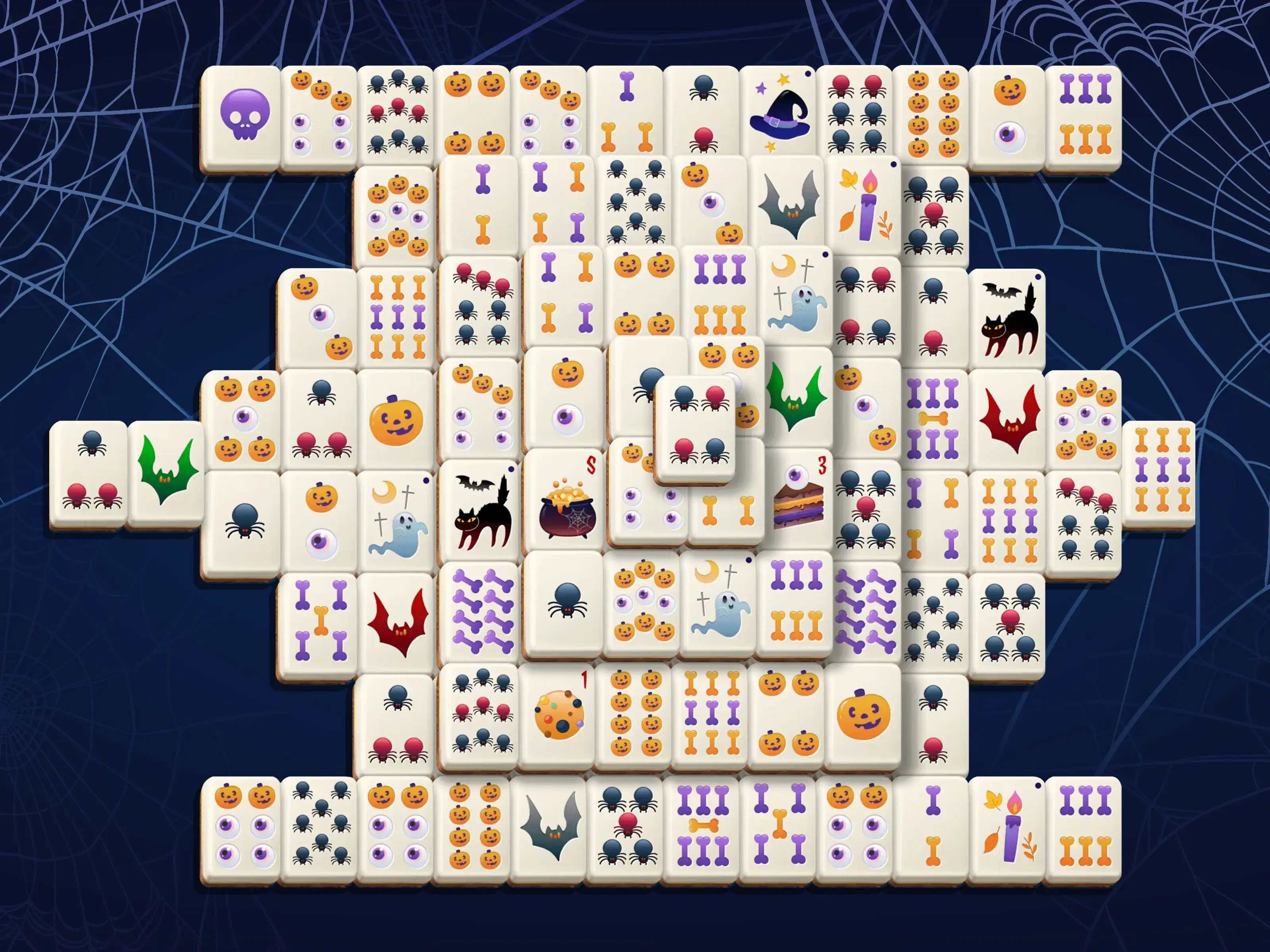 Preview image of the Halloween event on TheMahjong.com. The tiles are decorated with spooky elements such as bats, spiders, pumpkins, eyeballs, candles, witch hats, and ghosts. The dark blue background with spider webs enhances the festive atmosphere.